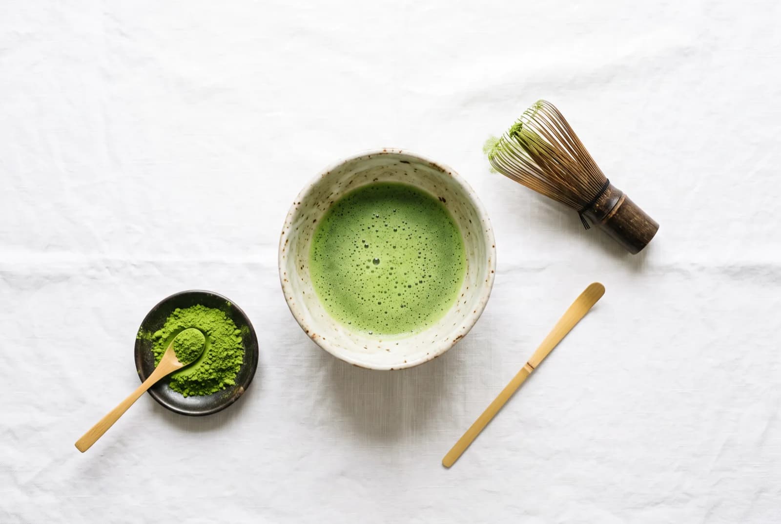 Bol chawan de matcha fouetté, fouet chasen, cuillère chashaku et matcha en poudre sur lin blanc